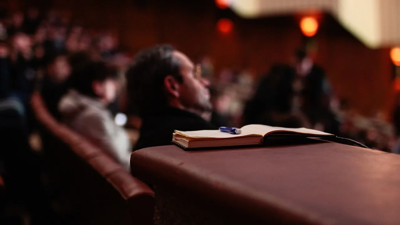 Une salle qui écoute une annonce, un carnet ouvert au premier rang